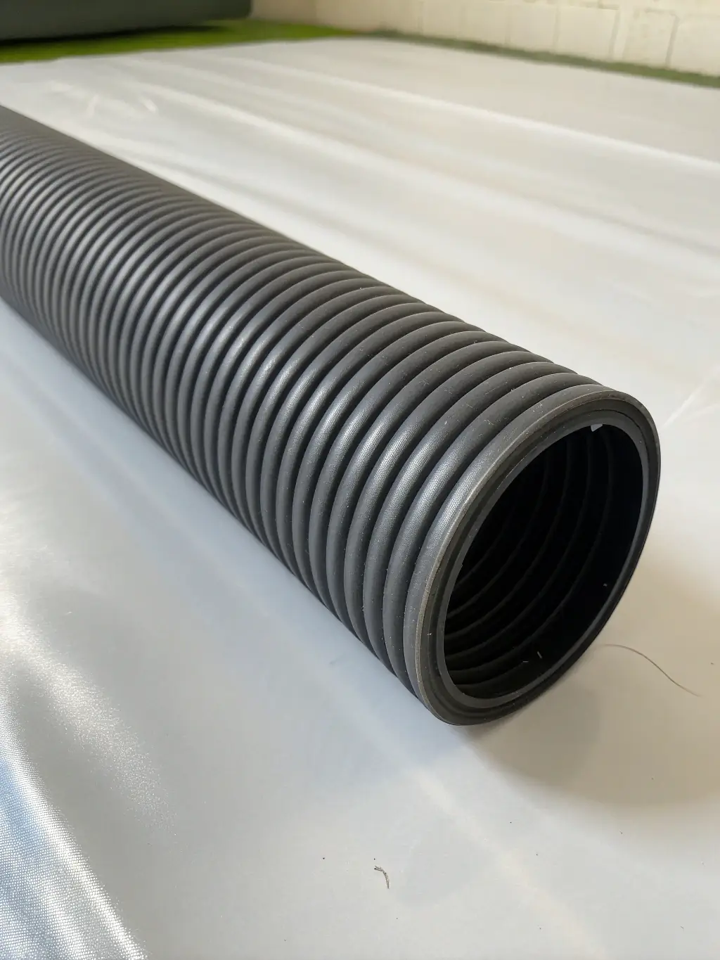 A close-up shot of a double-wall corrugated polyethylene pipe section, showcasing its robust construction and the interlocking design of the inner and outer layers. The pipe is yellow on the inside and black on the outside, highlighting its strength.
